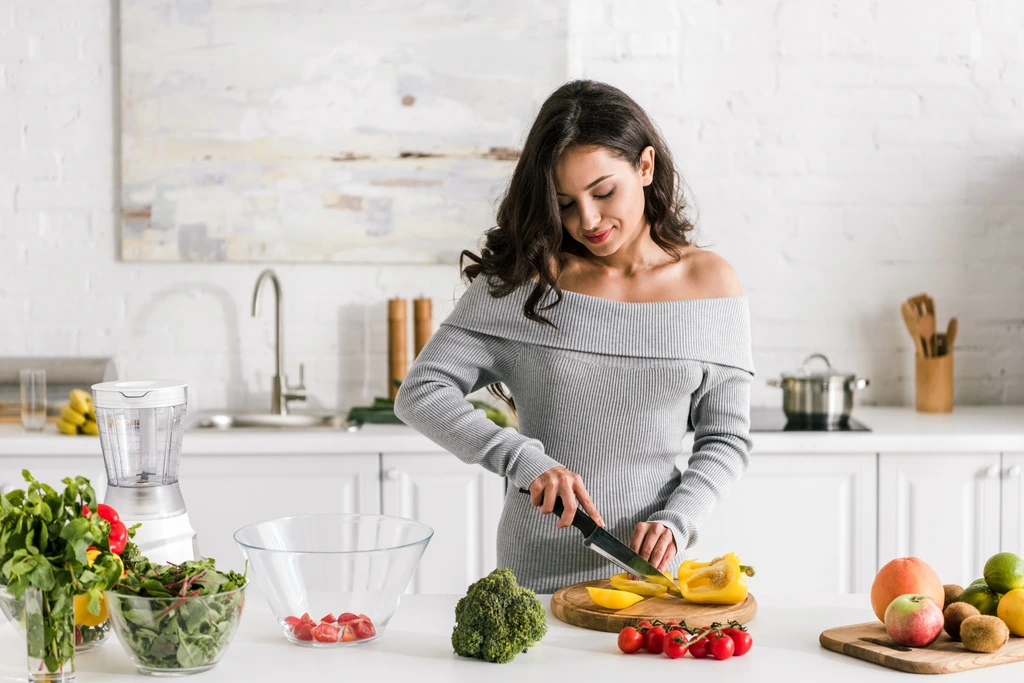 Elena Valdez carefully slicing a yellow bell pepper on a wooden cutting board, preparing a healthy one-dish meal.