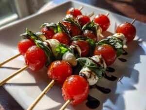 Close-up of several Caprese skewers featuring cherry tomatoes, mozzarella balls, and basil, drizzled with balsamic glaze.