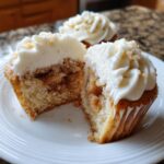 A close-up of one of the amazing Apple pie cupcakes cut in half, showing the spiced apple filling and cream cheese frosting.