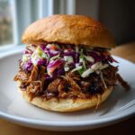 A close-up of a delicious BBQ pulled pork sandwich piled high with colorful coleslaw on a brioche bun.