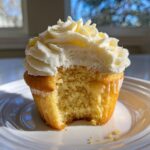 Close-up of a delicious lemon cupcake with a bite taken out, showing the moist crumb and thick white frosting.