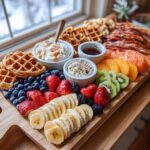 A stunning Breakfast Grazing Board featuring waffles, fresh berries, sliced bananas, kiwi, oranges, smoked salmon, and dips.