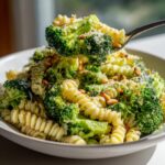 A fork lifting a bite of creamy Broccoli caesar pasta salad with fusilli pasta and bright green broccoli florets.