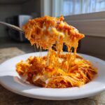 A spoonful of hot Buffalo chicken dip showing extreme cheese pull, served on a white plate.
