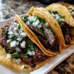 Close-up of several authentic Carne asada street tacos filled with grilled steak, topped with diced white onion and cilantro.