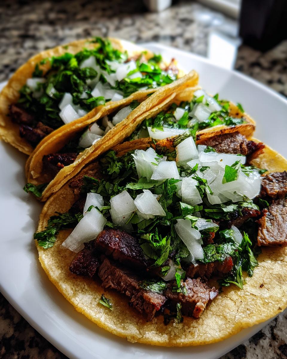 Close-up of three delicious carne asada street tacos topped with chopped white onion and cilantro.