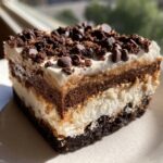 A decadent, layered slice of Chocolate chip cookie lasagna topped with whipped cream and mini chocolate chips.