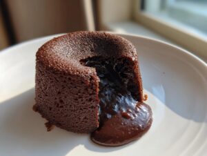 A freshly baked chocolate lava cake with the molten center oozing out onto a white plate.