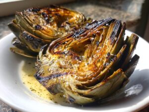 Close-up of two halves of classic grilled artichokes seasoned with salt and herbs, sitting in butter sauce.