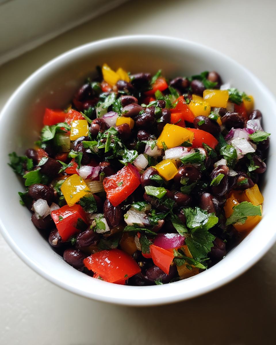 Close-up of vibrant Cowboy Caviar featuring black beans, diced red and yellow bell peppers, red onion, and cilantro in a white bowl.
