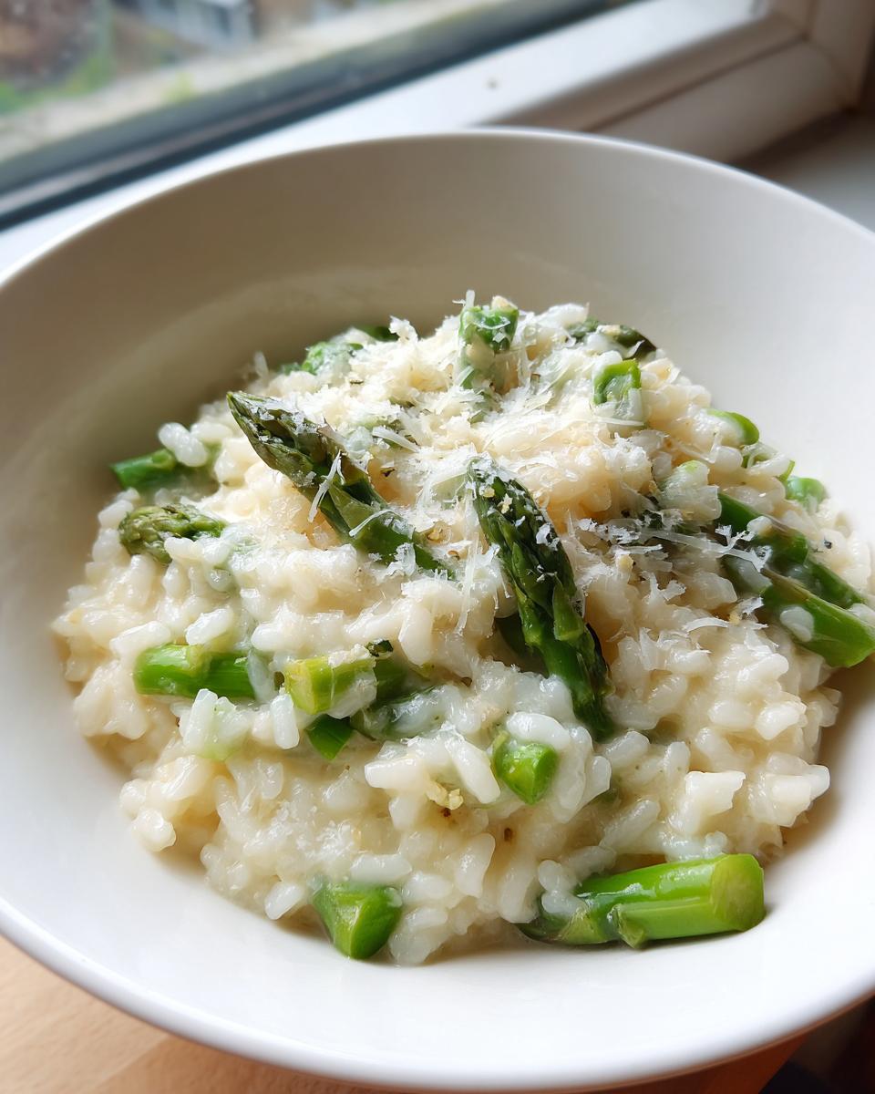 A close-up of creamy Asparagus Risotto in a white bowl, topped generously with grated Parmesan cheese and fresh asparagus tips.