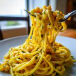 A fork lifts a generous twirl of bright yellow Creamy corn pasta mixed with corn kernels and green herbs.