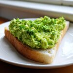 Close-up of a slice of white toast topped with a thick, bright green spread, likely the Benedictine sandwich filling.