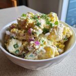 Close-up of a white bowl filled with creamy Southern potato salad, mixed with red onion and garnished with fresh dill.