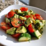 Close-up of vibrant Cucumber tomato avocado salad chunks tossed with fresh herbs in a white bowl.