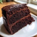 Close-up of a rich, dark slice of Devil's food cake with thick chocolate frosting on a white plate.