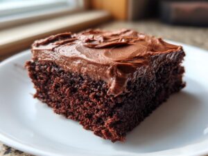 Close-up of a rich, dark slice of Devil's food sheet cake topped with thick chocolate frosting on a white plate.
