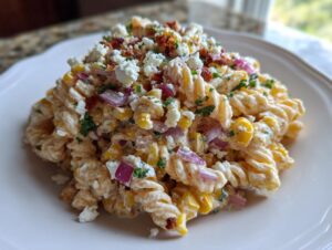 A mound of creamy Esquites pasta salad featuring rotini pasta, corn kernels, red onion, and crumbled white cheese.