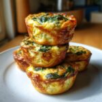 A stack of four golden-brown spinach mini quiches with a fluffy, eggy texture, served on a white plate.