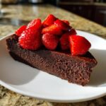 A rich slice of flourless chocolate torte topped generously with bright red roasted strawberries.