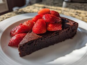 A rich slice of flourless chocolate torte topped generously with bright red roasted strawberries.