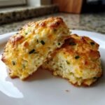 Two halves of a flaky, golden Savory cheddar biscuits topped with melted cheese and chives on a white plate.