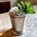 A frosty silver cup filled with crushed ice and a classic Mint Julep, garnished heavily with fresh mint sprigs.