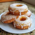 A stack of four golden baked apple pie donuts generously topped with a dripping vanilla glaze.