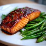 Close-up of a perfectly cooked piece of Sheet pan salmon with a dark, glossy glaze resting on a bed of bright green beans.