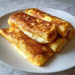 Close-up of several golden brown, pan-fried cheese blintzes rolled up and filled with creamy cheese filling.