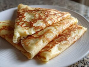 Close-up of golden brown Cheese Blintzes recipe items, folded and rolled, served on a white plate.