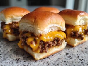 Close-up of several gooey Cheeseburger sliders featuring melted cheddar cheese over seasoned ground beef on soft buns.