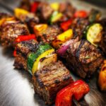Close-up of perfectly grilled lamb kabobs featuring charred cubes of meat alternating with zucchini, red onion, and bell peppers.