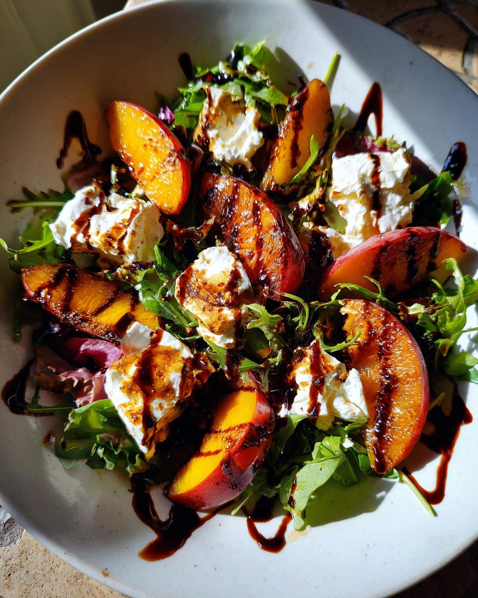 A vibrant bowl of grilled peach burrata salad featuring charred peach slices, creamy burrata cheese, and arugula drizzled with balsamic glaze.