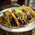 Three delicious grilled portobello tacos filled with dark, marinated mushroom slices and topped with fresh coleslaw.