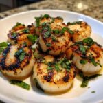 Close-up of perfectly seared grilled scallops with lemon and mint, resting in a white bowl.