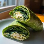 Two halves of a vibrant green Grogu spinach wrap cut in half, showing the filling of chicken, spinach, and creamy sauce.