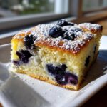 Close-up of a square slice of moist Lemon blueberry sheet pan pancakes, topped with fresh blueberries and powdered sugar.