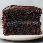 Close-up of a moist, dark slice of Devil's food cake showing two layers and rich chocolate frosting.