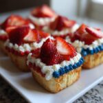 Close-up of Patriotic flag cupcakes decorated with white cream, red and blue frosting borders, and fresh sliced strawberries.