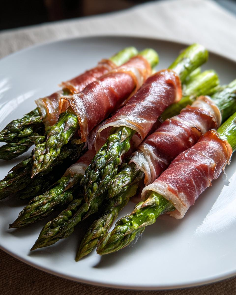 Close-up of perfectly cooked Prosciutto wrapped asparagus bundles resting on a white serving plate.