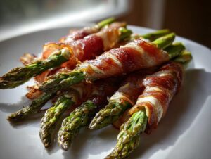 Close-up of several bundles of crispy Prosciutto wrapped asparagus spears resting on a white plate.