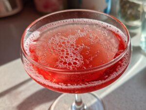 Close-up overhead view of a bright red, bubbly Raspberry lemonade mimosa served in a coupe glass.