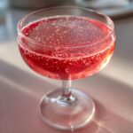 Close-up of a vibrant pink Raspberry lemonade mimosa sparkling in a shallow coupe glass.