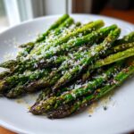 Close-up of bright green roasted asparagus spears topped generously with grated Parmesan cheese.