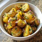 Close-up of vibrant yellow potato chunks tossed in a dressing with red onion and herbs, representing salt and vinegar potato salad.