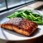 A perfectly cooked fillet of Sheet-pan miso honey salmon with a dark, shiny glaze, served alongside bright green snap peas.