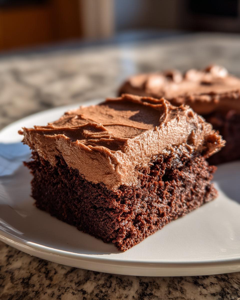 Close-up of a moist slice of Devil's food sheet cake topped with thick chocolate frosting on a white plate.