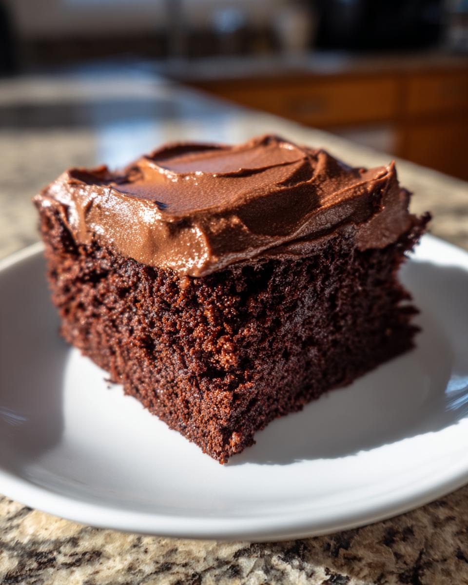 A close-up of a moist, dark chocolate slice of Devil's food sheet cake topped with thick chocolate frosting.