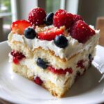 Close-up of a layered slice of Red white and blue berry trifle featuring cake, cream, strawberries, raspberries, and blueberries.